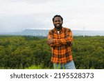 Portrait of black man smiling to camera at rural outdoor with wind turbine as background.