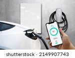 Home Charging Electric Vehicle With Cable Looking At App On Mobile Phone