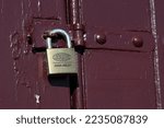 Small photo of Melbourne, Victoria, Australia - December 6 2022: Lockwood branded Assa Abloy padlock on a maroon painted door latch, keeping a wooden door locked shut