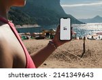 Small photo of Girl on the beach holding a smartphone with Nike Training Club NTC app on the screen. Rio de Janeiro, RJ, Brazil. March 2022.