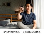 Portrait of happy 30s aged Asian man in casual clothing making facetime video calling with smartphone at home. He's waving at people on phone screen. Using conferencing meeting online app concept