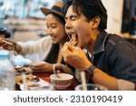 Small photo of Young Asian couple traveler tourists eating Thai street food together in China town night market in Bangkok in Thailand - people traveling enjoying food culture concept