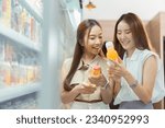 Small photo of Two beautiful Asian women shopping and checking items in supermarket. Female friends meeting and examining nutrition labels at convenient store