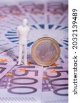 Small photo of The symbolic figure of a businessman made of plastic and a sonnet in denomination of 1 euro against the background of 500 euro bills