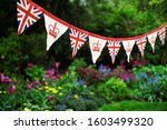 Banner of British Union Jack flag and royal crown celebratory bunting hanging in front of a bright English summer garden background