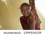 Small photo of Impishly Smiling Little African Girl Hugging a Tree Trunk