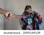 Veiled black African girl with her hand covering her eyes, pulled by the hand of an adult towards an atrocious fate; girl child abuse concept