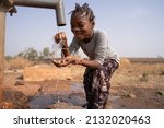 Small photo of Happy black little girl fooling around with water drops in front of a rough village tap; human right to water and sanitation concept