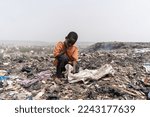 Small photo of Miserable hungry African slum child looking for edible and recyclable items in a huge urban garbage dump