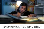 Small photo of Young focused school, college girl with pen in hand write, study, think, doing assignment project homework for exams. Hard working Indian teen concentrating, read alone late hours in night at home