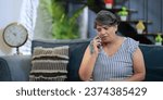 Small photo of Upset Indian old grey-haired woman sitting on sofa talking on mobile phone answer unpleasant call received bad shocking news. Disappointed worried senior grandmother feel sadness alone at indoor home