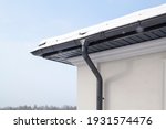 Corner of the house with new gray metal tile roof and rain gutter at winter. Metallic Guttering System, Guttering and Drainage Pipe Exterior