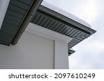 Small photo of Corner of the house with new gray metal tile roof and rain gutter covered by snow at winter. Metallic Guttering System, Guttering and Drainage Pipe Exterior