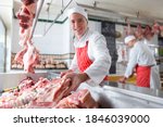 A young butcher smiling and holding meat near the camera in a meat shop.