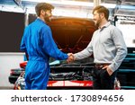 The mechanic shaking hands with customer after finish checking the opened hood red car. Focus on happy mechanic and satisfied customer. Auto car repair service center. Professional service.