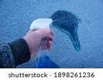 Removal ice from automobile windshield. Hand with liquid spray for car window defrost in winter season. 