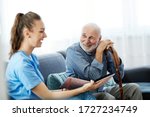 Doctor or nurse caregiver with senior man looking at photo album and picture  at home or nursing home