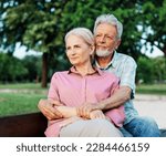 Small photo of Portrait of happy ctive senior couple daydreaming and relaxing sitting on a bench in park outdoors