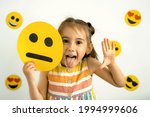 Small photo of World emoji day. A funny girl holds a cardboard happy smiley face in her hands and shows her tongue while laughing. Temperament: choleric, melancholic, sanguine, phlegmatic.