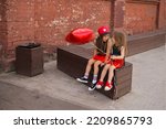 Small photo of Two little girl friends dressed in rock style with balloon in shape of star are sitting on bench in an abandoned area of city and having fun chatting. Conversations and twaddle of two sisters