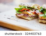 Healthy sandwich made of a fresh seeded roll, cut in half to display tasty ingredients of salami, tomato, lettuce and chess, presented on a wooden board