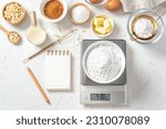 Small photo of Flour in bowl on digital scale with notepad and pen and baking ingredients, flour, nuts, eggs, sugar, milk and gold whisk on marble table, flatlay