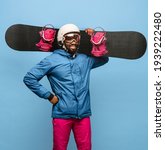Small photo of Portrait of happy man snowboarder with snowboard, ski helmet and goggles in bright ski suit posing isolated on blue background. Concept of human emotions, sport and healthy life. Copy space for ad.