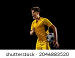 After winning game. Happy proud male football player in yellow uniform isolated over dark background. Successful competition. Concept of action, speed, energy, sport, competition and ad.