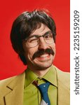 Small photo of Close-up portrait of man with moustache posing in vintage suit and glasses isolated over red background. Winking. Concept of retro style, creativity, emotions, facial expression, fashion, occupation