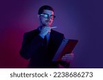 Young man, manager wearing business suit and eyeglasses using digital tablet on gradient blue purple background in neon light. Studying, online work, job, finance, new app concept