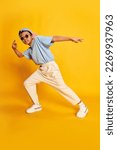 Small photo of Dynamic portrait of little african boy, hip-hop dancer in stylish street style clothes dancing over bright yellow background. Concept of music, dance happiness. Kid looks happy and sportive
