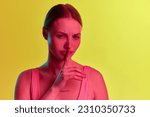 Small photo of Gossips, secret. Charming young girl showing willingness to tell something new over yellow-orange background in neon light. Concept of beauty, youth, human emotions, mood, ad, sales, news