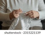 Small photo of Old woman's hands knitting with crochet hook. Grandma crocheting with white thread a lace tablecloth. Handicraft concept
