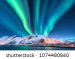 Aurora borealis. Lofoten islands, Norway. Aurora. Green northern lights. Starry sky with polar lights. Night winter landscape with aurora, sea with sky reflection and snowy mountains.Nature background
