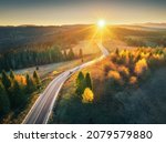 Small photo of Aerial view of mountain road in forest at sunset in autumn. Top view from drone of road in woods. Beautiful landscape with roadway in hills, pine trees, green meadows, golden sunlight in fall. Travel