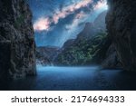 Milky Way over the beautiful mountain canyon and blue sea at night in summer. Colorful landscape with bright starry sky with Milky Way, rocks, trees, moonlight, fog, water. Galaxy. Nature and space