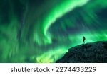 Small photo of Northern lights and young woman on mountain peak at night. Aurora borealis and silhouette of alone girl on top of rock. Landscape with polar lights. Starry sky with bright aurora. Travel background