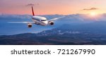 Passenger airplane. Landscape with white airplane is flying in the orange sky with clouds over mountains, sea at colorful sunset. Passenger aircraft is landing. Commercial plane. Private jet. Travel