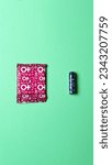 Small photo of A sanitary napkin and a tampon lie on a green background. View from above. Gasket in red packaging. A tampon in a lilac package. Vertical image. Flatley