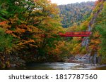 Scenery of the red Futami suspension bridge over Toyohira River with beautiful fall colors on the riverside cliffs in Jozankei (定山渓), a famous Onsen (hot spring) destination in Sapporo Hokkaido, Japan