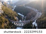 Small photo of Aerial view of a train traveling on famous Kalte Rinne Viaduct of Semmering Railway line to enter a tunnel in the rocky cliff of alpine mountains with snow in the deep gorge, in Breitenstein, Austria