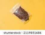 Roasted arabica coffee beans in blank transparent plastic bag with zipper on yellow background. Specialty and alternative sample coffee trendy concept. Mock up, top view, flat lay, isolated