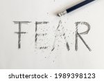Small photo of Erasing fear. Fear written on white paper with a pencil, erased with an eraser. Symbolic for overcoming fear or treating fear.
