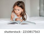 Emotional child girl read interesting book in bed. Small kid enjoy reading new facts pointing finger. Developing child fantasy and imagination. Imaginary world. Fairy tale. Bedtime reading