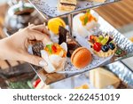 Small photo of English Afternoon Tea delights with sweet breakfast snacks. Ceremony showcases beautiful desserts and treats. A woman hand selects a dessert from the tea stand.