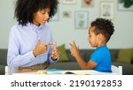 Small photo of A smart boy counts on his fingers, studies with a private teacher in the office, a child learns numbers and how to count, sits at a table with a tutor