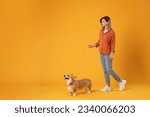 Small photo of Walk with pet. Excited young lady walking with her cute corgi dog on a leash isolated on yellow studio background, full body length, banner, free space