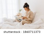 Side view of woman sitting on bed using laptop computer. Woman making online transaction using credit card sitting at home.