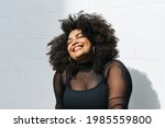 Happy woman in fashionable wear standing near wall. Pretty female in black outfit on white background.