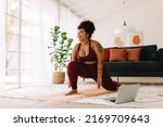 Plus size woman following workout video on laptop and doing home workout. Happy female in workout wear stretching at home.